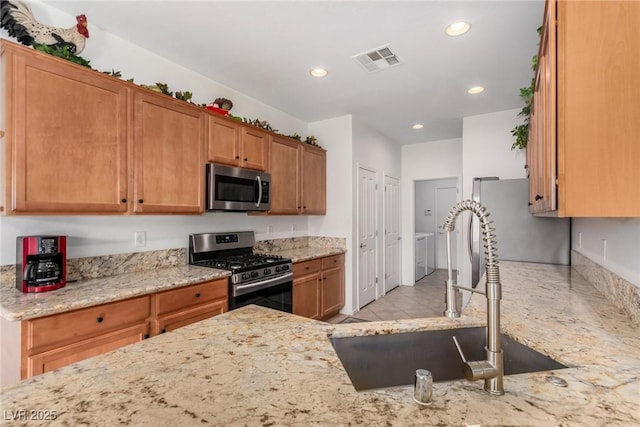 kitchen with stainless steel appliances, a sink, washer and dryer, light stone countertops, and recessed lighting