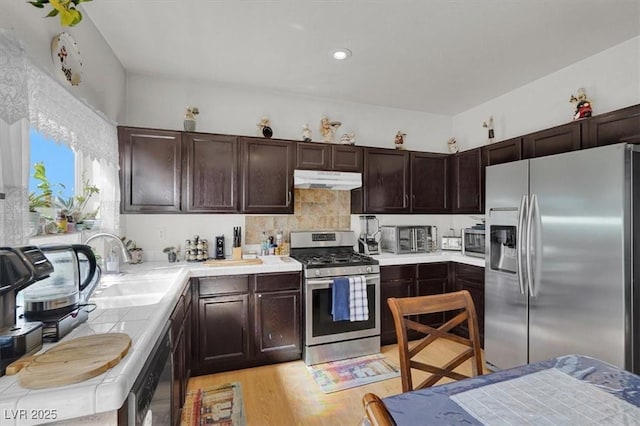 3389 Commendation Dr, Las Vegas, NV 89117 - kitchen with appliances with stainless steel finishes, dark brown cabinetry, under cabinet range hood, light wood-style floors, and tile countertops
