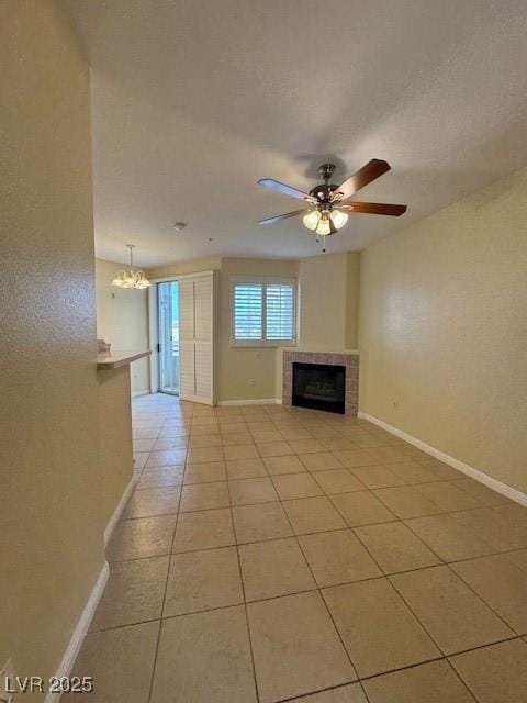 unfurnished living room featuring a tile fireplace, light tile patterned floors, baseboards, a ceiling fan, and a chandelier