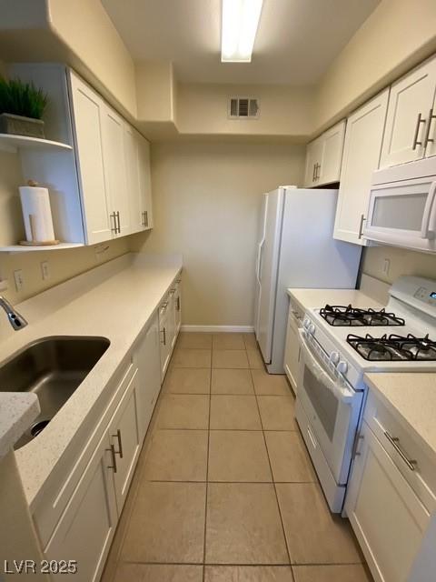 kitchen with white appliances, a sink, white cabinetry, light tile patterned floors, and light countertops