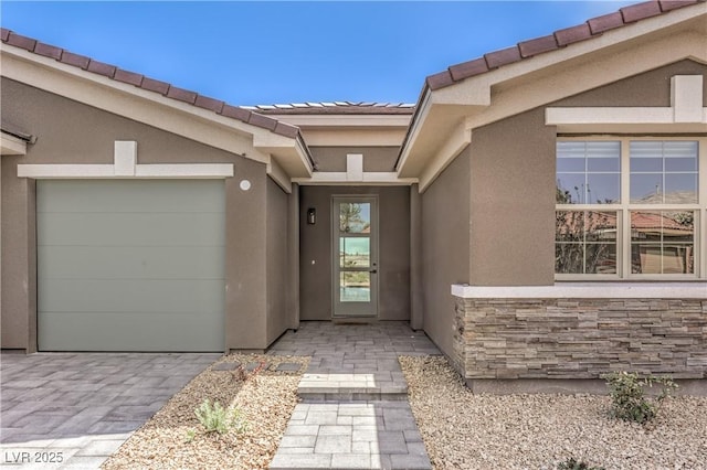 property entrance featuring stucco siding, a tile roof, an attached garage, and driveway