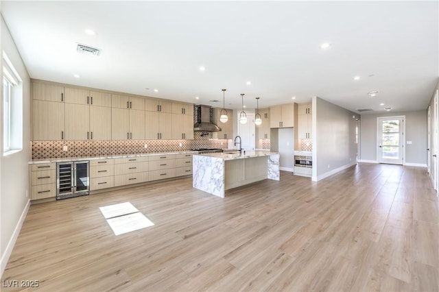 kitchen with wine cooler, wall chimney range hood, a sink, tasteful backsplash, and recessed lighting