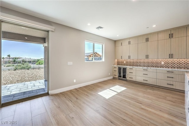 kitchen with beverage cooler, tasteful backsplash, light wood-type flooring, light countertops, and baseboards