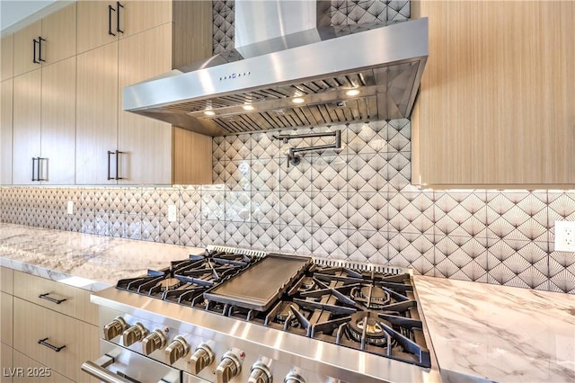 kitchen featuring wall chimney range hood, gas stove, backsplash, and light stone countertops