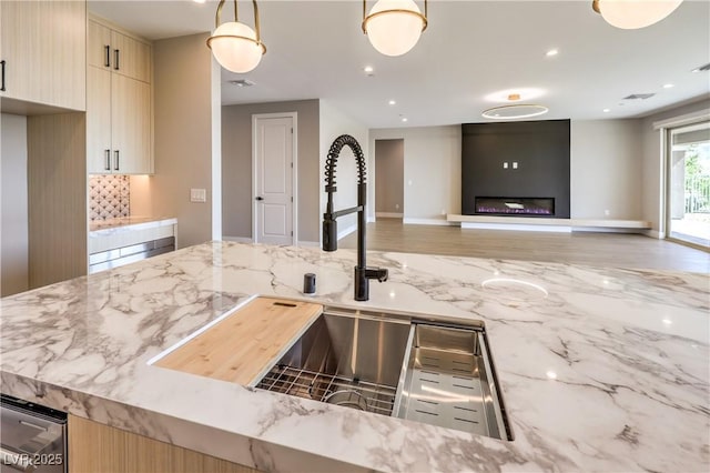 kitchen with a sink, light stone counters, light brown cabinetry, backsplash, and recessed lighting
