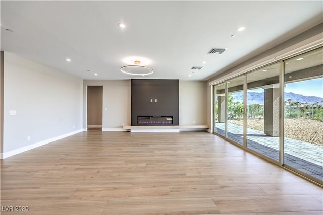 unfurnished living room featuring baseboards, light wood finished floors, recessed lighting, a large fireplace, and a mountain view