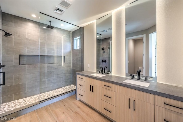 bathroom featuring a tile shower, double vanity, and wood finished floors