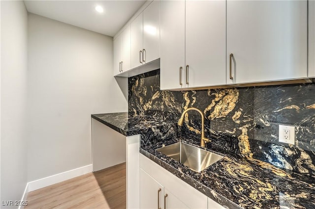 kitchen with a sink, light wood finished floors, baseboards, decorative backsplash, and white cabinets
