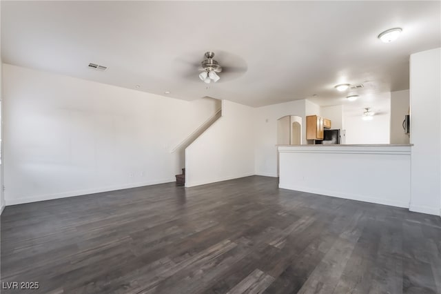 unfurnished living room featuring ceiling fan, dark wood-type flooring, stairway, and arched walkways