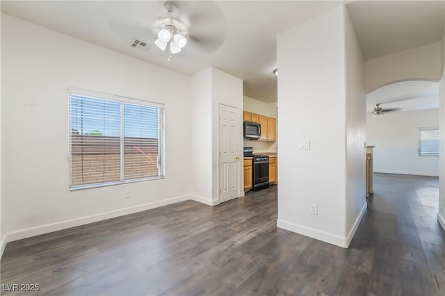 unfurnished living room featuring ceiling fan, arched walkways, dark wood-style flooring, and baseboards