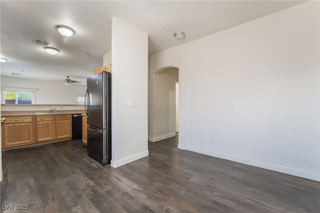 kitchen with freestanding refrigerator, arched walkways, black dishwasher, dark wood-style flooring, and brown cabinetry