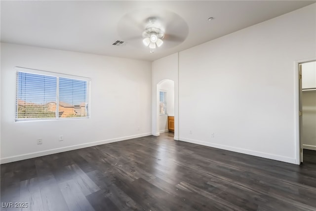 unfurnished bedroom with arched walkways, dark wood finished floors, baseboards, a walk in closet, and ceiling fan