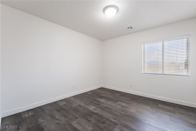 spare room with baseboards and dark wood-type flooring
