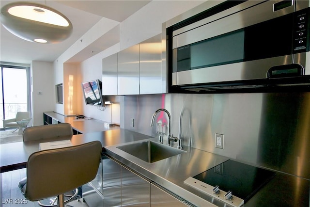 kitchen featuring stainless steel countertops, stainless steel microwave, a sink, modern cabinets, and white cabinets