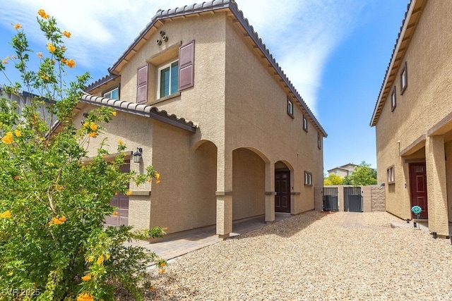 view of property exterior featuring a tile roof, stucco siding, cooling unit, a gate, and fence