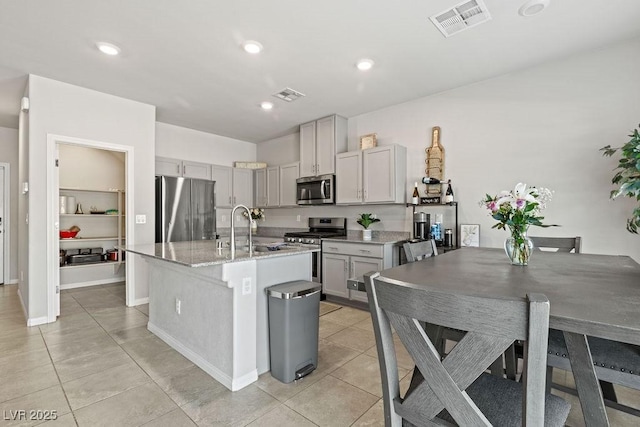 kitchen featuring stainless steel appliances, a sink, light tile patterned floors, an island with sink, and gray cabinetry