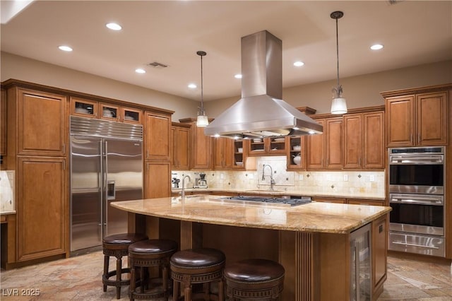 8620 W La Madre Way, Las Vegas, NV 89149 - kitchen featuring appliances with stainless steel finishes, island exhaust hood, a warming drawer, brown cabinets, and beverage cooler