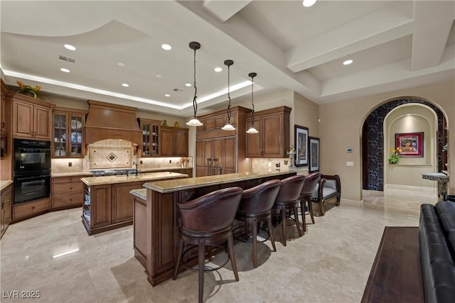 5079 Mountain Top Cir, Las Vegas, NV 89148 - kitchen with a tray ceiling, custom range hood, arched walkways, decorative backsplash, and a center island with sink