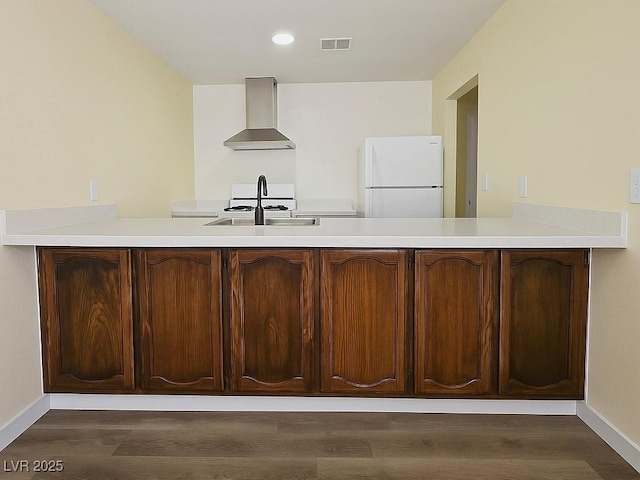 kitchen featuring wall chimney exhaust hood, freestanding refrigerator, a peninsula, baseboards, and dark wood-style flooring