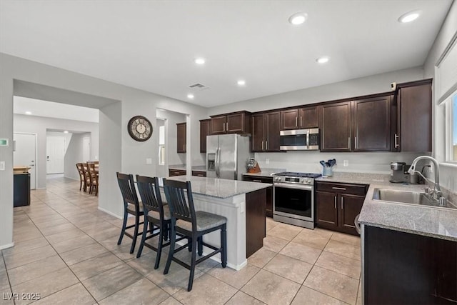 kitchen with appliances with stainless steel finishes, a sink, light tile patterned floors, a kitchen breakfast bar, and a center island