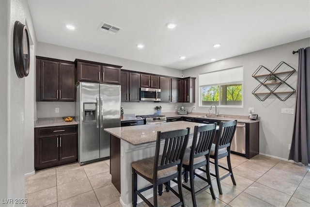 kitchen with stainless steel appliances, dark brown cabinets, light tile patterned floors, a center island, and recessed lighting