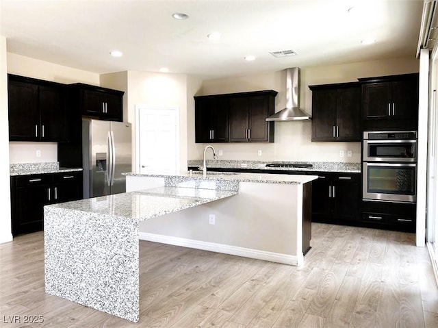 7861 Hamilton Pool Dr, Las Vegas, NV 89113 - kitchen with appliances with stainless steel finishes, wall chimney range hood, a sink, a center island with sink, and light wood-style flooring