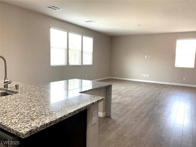 7861 Hamilton Pool Dr, Las Vegas, NV 89113 - kitchen featuring light wood finished floors, light stone countertops, baseboards, a sink, and a kitchen island with sink
