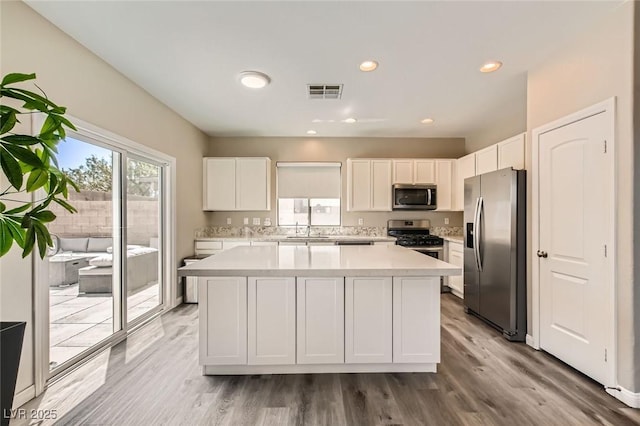 8469 Cheerful Brook Ave, Las Vegas, NV 89143 - kitchen with stainless steel appliances, light countertops, a kitchen island, white cabinetry, and light wood-style flooring