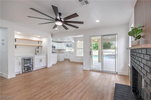 2107 Fountain Springs Dr, Henderson, NV 89074 - unfurnished living room featuring wine cooler, a brick fireplace, ceiling fan, light wood-style floors, and baseboards
