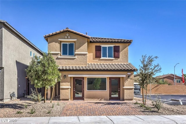 mediterranean / spanish house featuring a tile roof, stucco siding, fence, and a patio