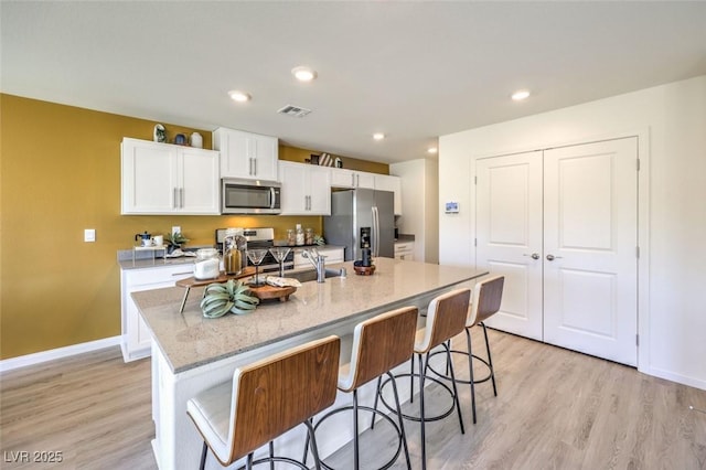 kitchen with appliances with stainless steel finishes, a sink, white cabinetry, light wood-style floors, and a center island with sink