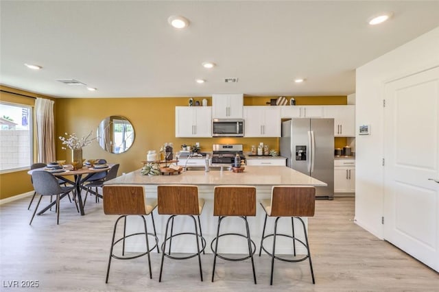 kitchen with appliances with stainless steel finishes, a breakfast bar area, white cabinets, and recessed lighting