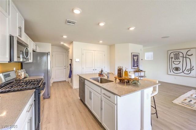 kitchen with appliances with stainless steel finishes, a sink, light wood finished floors, a breakfast bar, and recessed lighting