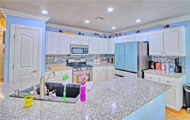 kitchen with appliances with stainless steel finishes, white cabinetry, a sink, crown molding, and tasteful backsplash