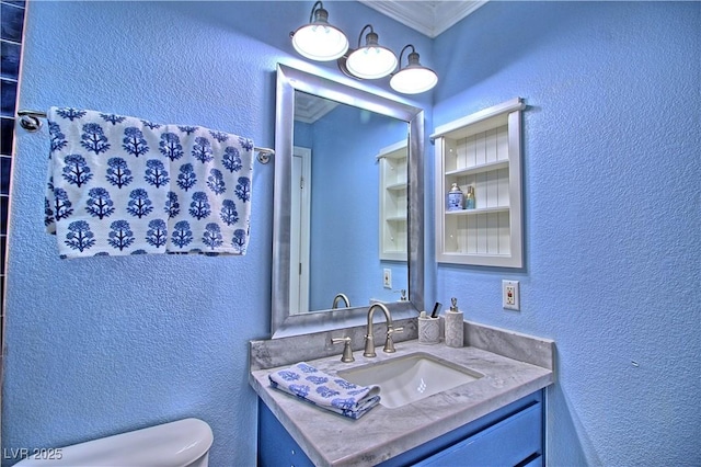 bathroom with toilet, a textured wall, vanity, and ornamental molding
