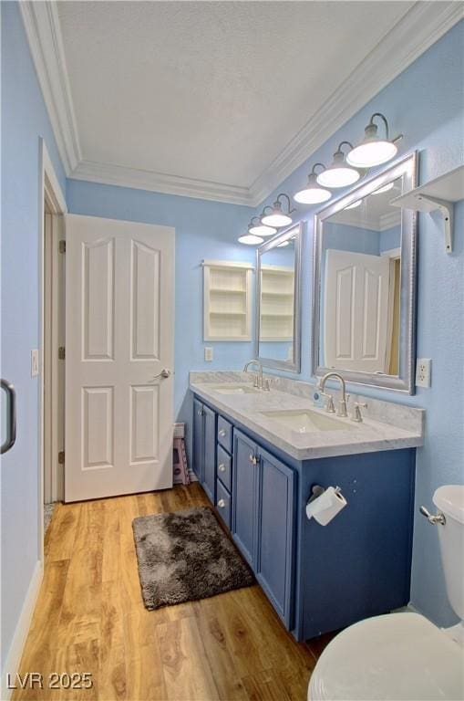bathroom featuring toilet, wood finished floors, crown molding, and double vanity
