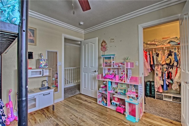 playroom featuring ornamental molding, wood finished floors, a ceiling fan, and a sink