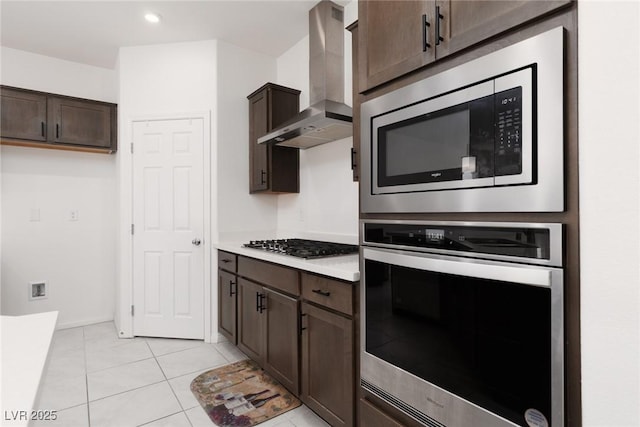 kitchen featuring wall chimney exhaust hood, appliances with stainless steel finishes, dark brown cabinetry, light countertops, and light tile patterned floors