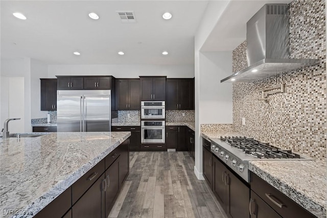 11088 Westcroft Way, Las Vegas, NV 89183 - kitchen with stainless steel appliances, wall chimney range hood, a sink, light wood-style flooring, and light stone counters