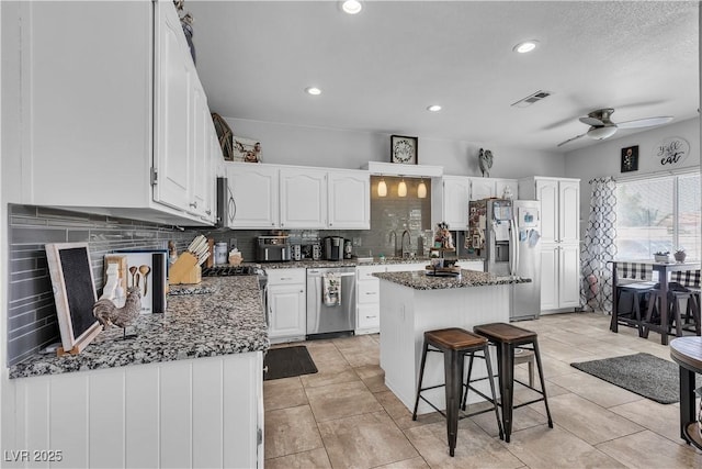 7929 Ben Hogan Dr, Las Vegas, NV 89149 - kitchen featuring stainless steel appliances, backsplash, white cabinets, a ceiling fan, and a kitchen island