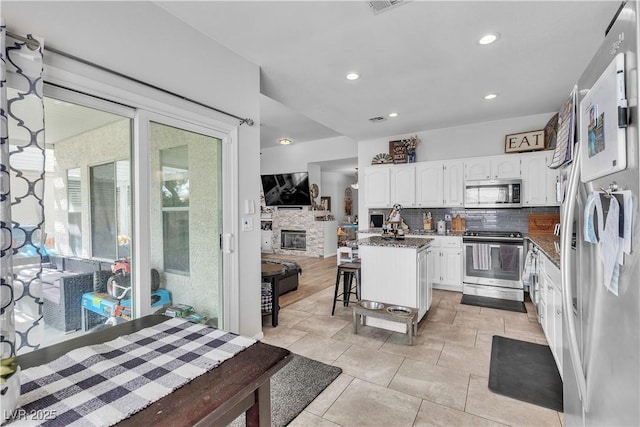 7929 Ben Hogan Dr, Las Vegas, NV 89149 - kitchen featuring appliances with stainless steel finishes, white cabinetry, backsplash, a fireplace, and dark stone counters