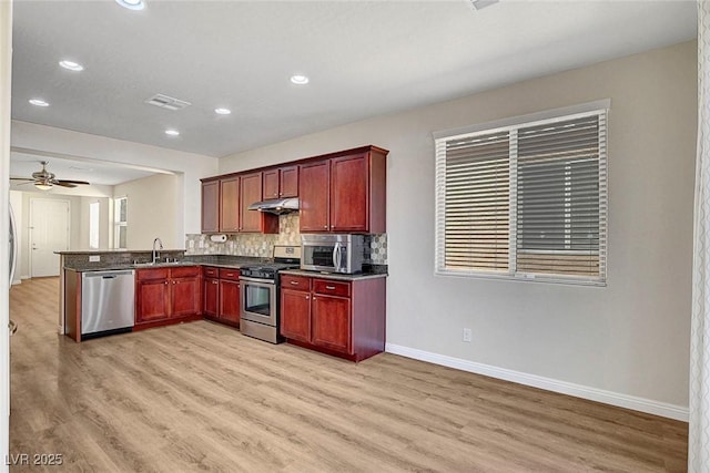 248 Windmill Croft Dr, Las Vegas, NV 89148 - kitchen with stainless steel appliances, a sink, under cabinet range hood, dark countertops, and light wood finished floors