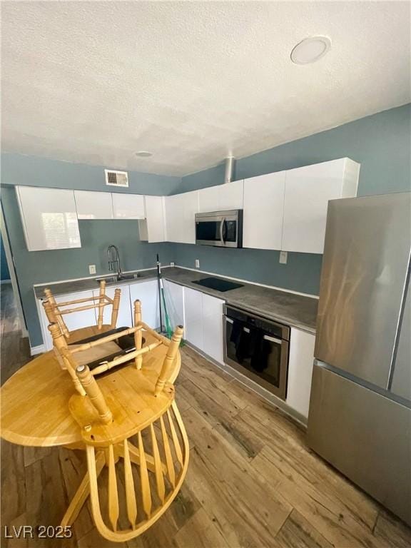 501 S Maryland Pkwy Unit C17, Las Vegas, NV 89101 - kitchen featuring appliances with stainless steel finishes, white cabinets, light wood-style flooring, a sink, and a textured ceiling