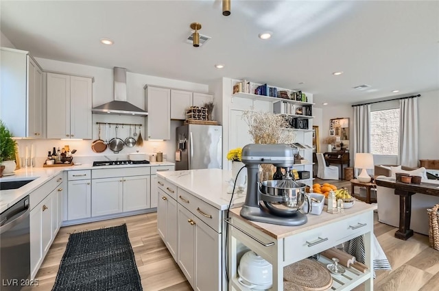 kitchen with appliances with stainless steel finishes, wall chimney range hood, light countertops, light wood-type flooring, and recessed lighting
