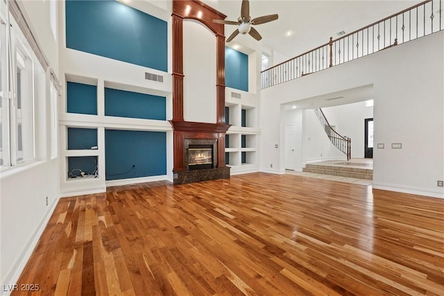 unfurnished living room with wood finished floors, built in shelves, ceiling fan, and a high ceiling