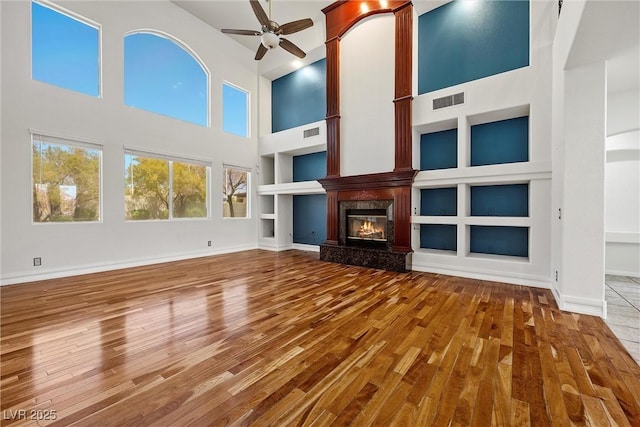 unfurnished living room featuring built in features, ceiling fan, wood finished floors, a premium fireplace, and a high ceiling