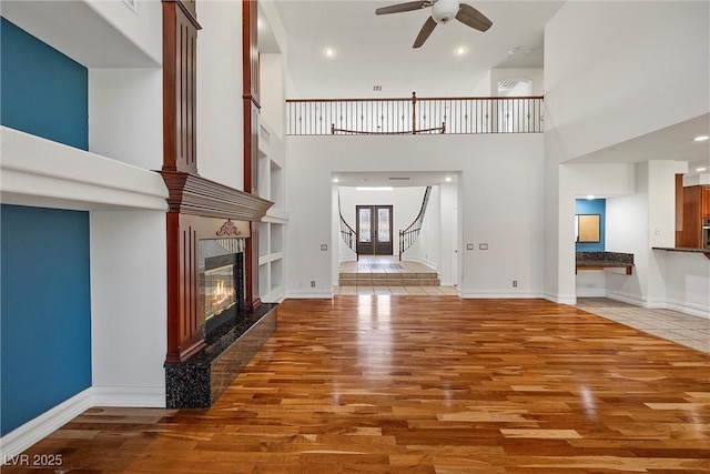 unfurnished living room featuring a ceiling fan, wood finished floors, a fireplace, a towering ceiling, and stairs