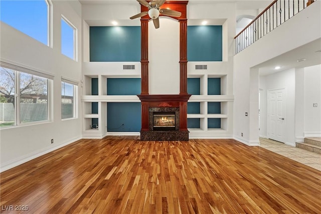 unfurnished living room featuring built in shelves, a high ceiling, wood finished floors, ceiling fan, and a fireplace