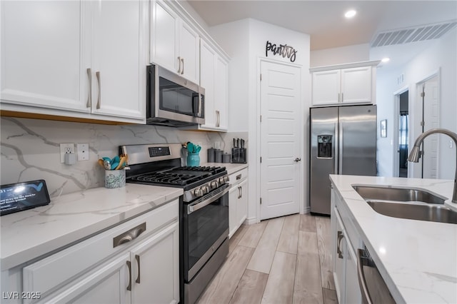 778 Dainty Daffodil St, Henderson, NV 89011 - kitchen with stainless steel appliances, a sink, white cabinets, tasteful backsplash, and light wood-style floors
