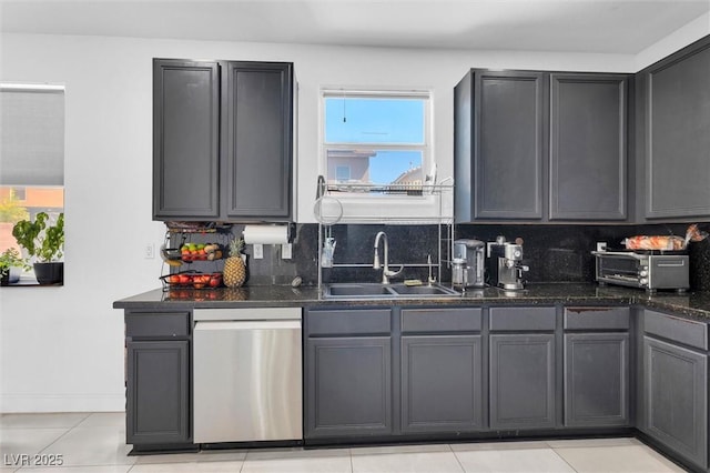 kitchen featuring stainless steel dishwasher, a sink, backsplash, light tile patterned flooring, and dark stone counters